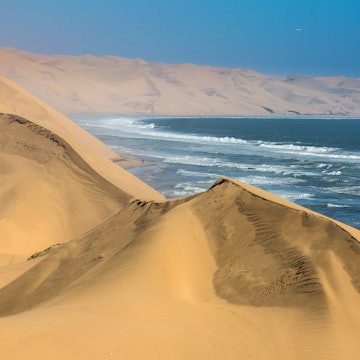 The concept of extreme and exotic tourism. Ocean surf with foamy waves. Gorgeous jeep - safari through the huge sand dunes. Atlantic coast of Walvis Bay, Namibia, south of Africa